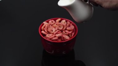 Macro vuruldu. Sarı mısır gevrekleri taze sütle doludur. Kase masanın üstünde, siyah arka planda..