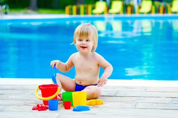 Toddler by the pool palying with toy bucket set — Stock Photo, Image