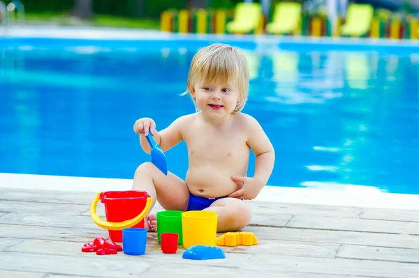 Toddler by the pool palying with toy bucket set — Stock Photo, Image