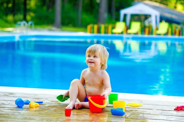 Toddler by the pool palying with toy bucket set — Stock Photo, Image