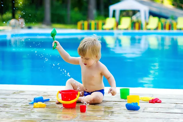 Cute kid playing with toy bucket set by the pool — Stock Photo, Image