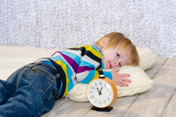 Tired toddler lying down with alarm clock in front — Stock Photo, Image