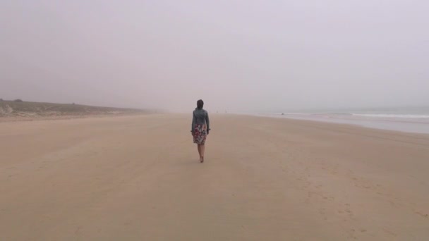 Женщина в джинсовой куртке идет на туманный пляж 60 — стоковое видео