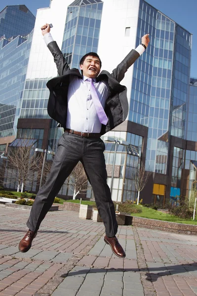 Jumping happy businessman over office buildings background — Stock Photo, Image