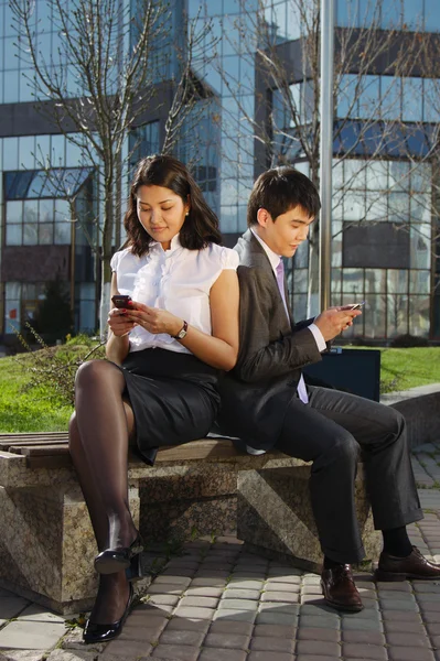 Firmy para siedzi na ławce rozmowy z telefonu komórkowego — Zdjęcie stockowe