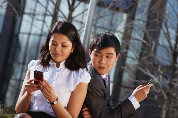 Business couple sitting on the bench chatting with mobile phone — Stock Photo, Image