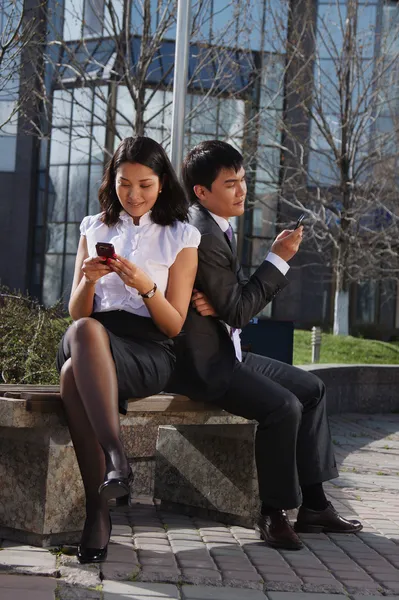 Business couple sitting on the bench chatting with mobile phone — Stock Photo, Image