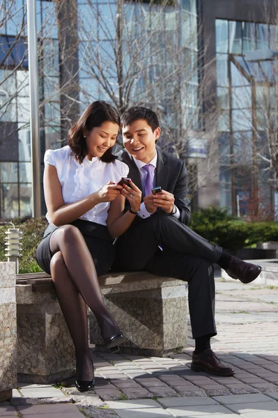 Business couple sitting on the bench chatting with mobile phone — Stock Photo, Image