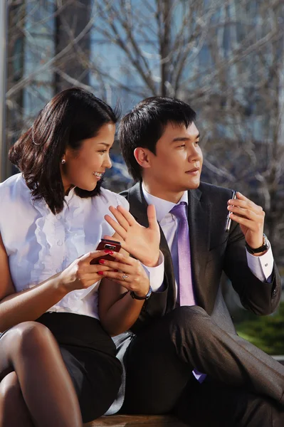 Business couple sitting on the bench chatting with mobile phone — Stock Photo, Image