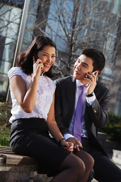 Business couple sitting on the bench chatting with mobile phone — Stock Photo, Image