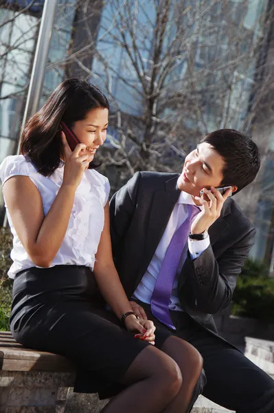 Business couple sitting on the bench chatting with mobile phone — Stock Photo, Image