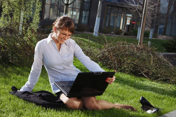 Femme couchée sur l'herbe avec ordinateur portable avec bâtiment d'affaires sur le dos — Photo