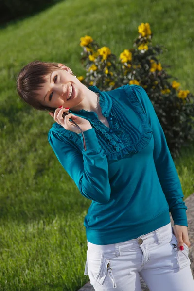 Krásná usměvavá dívka rozhovory na mobilní telefon venku — Stock fotografie