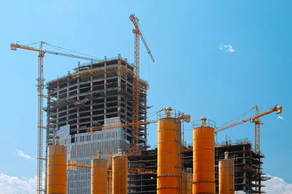 Edifícios altos em construção com guindastes contra um céu azul — Fotografia de Stock