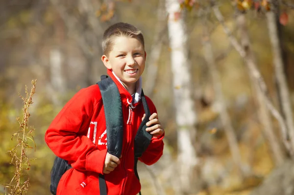 Fericit băiat excursionist zâmbitor cu rucsac în pădure. Îmbrăcat în roșu — Fotografie, imagine de stoc