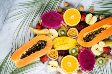 Bir grup egzotik tropikal meyve. Papaya, mango, ejderha meyvesi, çarkıfelek meyvesi, kivi, çilek, elma, muz, portakal, longan, yeşil yapraklar beyaz arka planda.