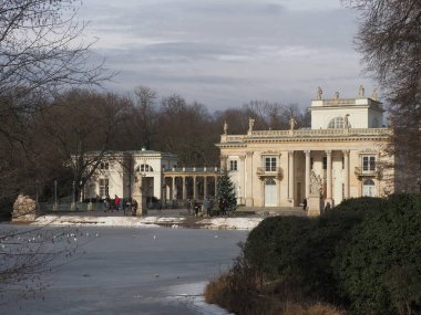 Polonya 'nın Masovian Voyvoda, Varşova' nın başkenti Varşova 'daki hamam parkında, adanın yanındaki donmuş göl, 2019 soğuk kış gününde bulutlu gökyüzü.