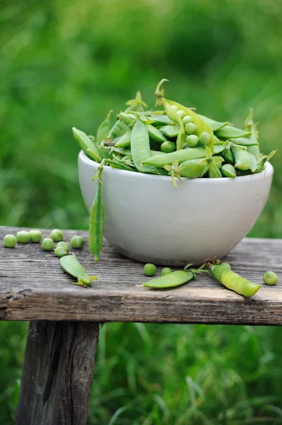Čerstvý zelený hrášek v bílé misce na dřevěný stůl — Stock fotografie