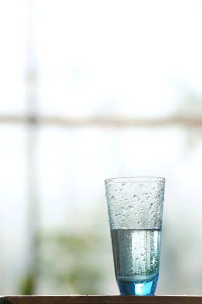 Glass of cold mineral water on the table in front of window — Stock Photo, Image