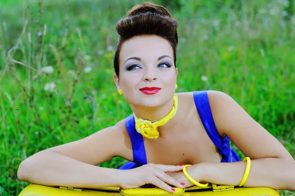 Menina feliz sorridente bonita em um vestido azul com uma mala amarela está descansando em uma grama verde — Fotografia de Stock