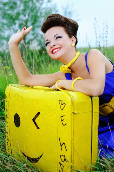 Schöne lächelnde Mädchen in einem blauen Kleid mit einem gelben Koffer auf der Straße — Stockfoto