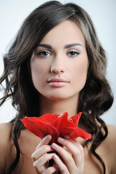 Krásná žena s čerstvým zdraví kůže obličeje a červený květ v ruce — Stock fotografie
