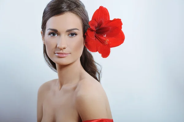 Mulher bonita com pele de saúde fresca de rosto e flor vermelha no cabelo — Fotografia de Stock