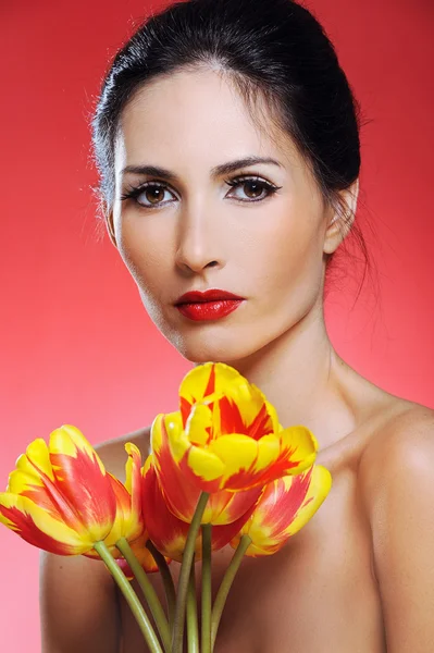 Mujer bonita sosteniendo un montón de tulipanes sobre fondo rojo — Foto de Stock