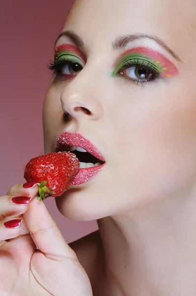 Close up young girl with bright makeup eating strawberry — Stock Photo, Image