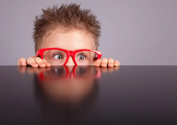 Carino ragazzo nascosto dietro un tavolo Fotografia Stock