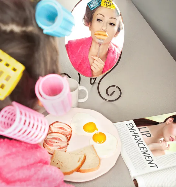 Woman with sausages on a fork simulating lip enhancement while having breakfast — Stock Photo, Image