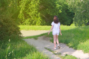 Beyazlı bir kız ormanda kır yolu boyunca yürüyor ve yeşil çimenler içinde..