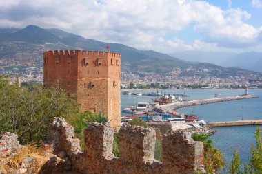 Hindi. Antalya. 09.15.21. Akdeniz kıyısındaki tatil köyünün manzarası. Dağların yamaçlarında evler ve eski bir kale duvarı..