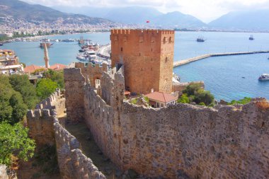 Hindi. Antalya. 09.15.21. Akdeniz kıyısındaki tatil köyünün manzarası. Dağların yamaçlarında evler ve eski bir kale duvarı..