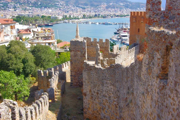 Hindi. Antalya. 09.15.21. Akdeniz kıyısındaki tatil köyünün manzarası. Dağların yamaçlarında evler ve eski bir kale duvarı..