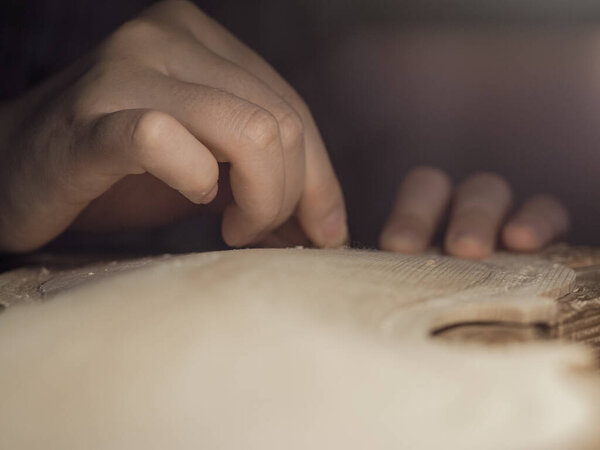 artisan working on raw wood violin plate with finger plane on the bench