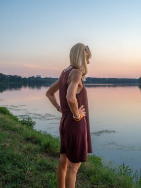 Güzel bir kadın gün batımında nehrin kenarında tatilin tadını çıkarır.