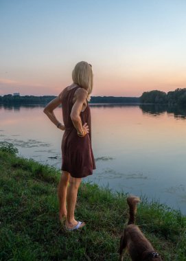 Güzel bir kadın gün batımında nehrin kenarında tatilin tadını çıkarır.