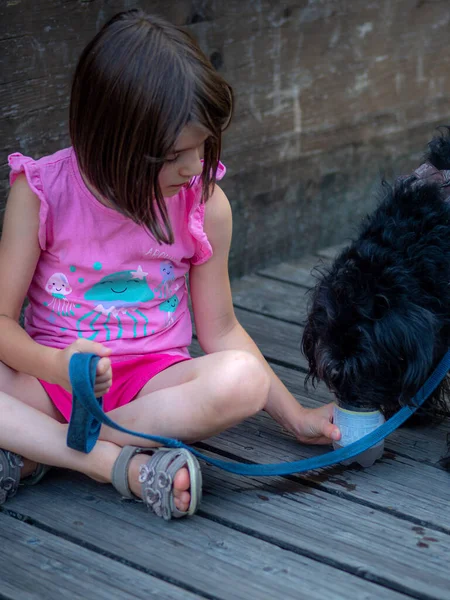 girl waterng her dog outdoors with a plastic recycled water bottle