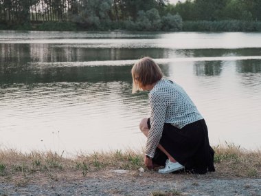 senior lady relaxing in the park wearing sunglasses near the river bank in summer