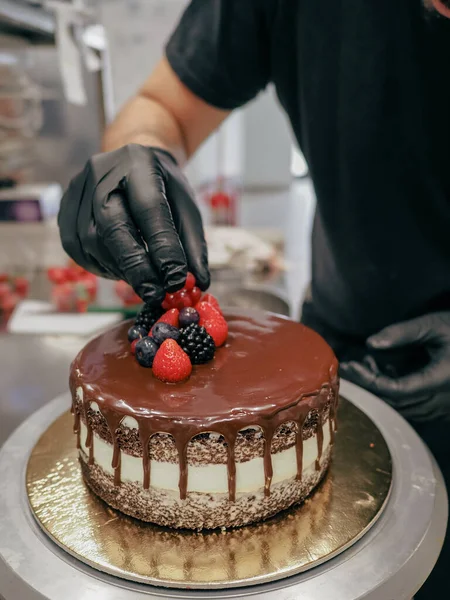 hand of chef toppig a choco cake with gold and berries in the lab