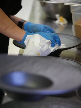 Eldiven takmış, makarnayı servis eden ve dekore eden bir şefin yakın çekimi.