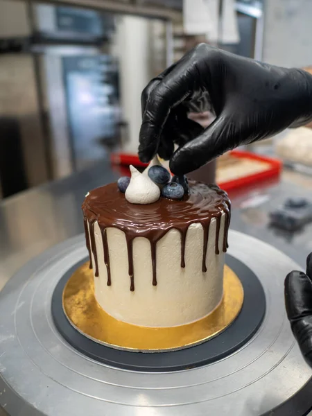 unrecognizable worker preparing a sweet dripping choco cake and berries