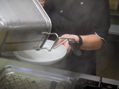 Beyaz üniformalı şef tavaya sebzeli makarna pişirmek için haşlanmış spagetti dolduruyor.