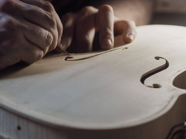 Close up of professional master artisan luthier painstaking detailed work on wood violin in a workshop.