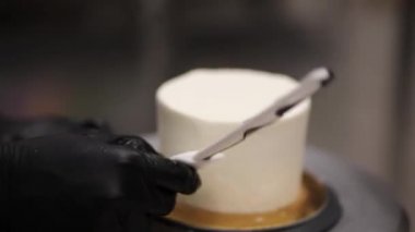 Süslü pasta üzerindeki tereyağını yumuşatmak için spatula ve kazıyıcı kullanıyor.