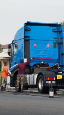 Adam, oto yıkamacıdaki self servis ekipmanlarını kullanarak mavi kamyonun dışını spreyliyor..