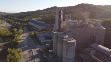 Mavi bulutlu arka planda depoları olan çimento üretim tesisinin havadan görüntüsü. Stok görüntüleri. Endüstriyel bölge ve çimento üretim fabrikasının üzerinde uçuyor.