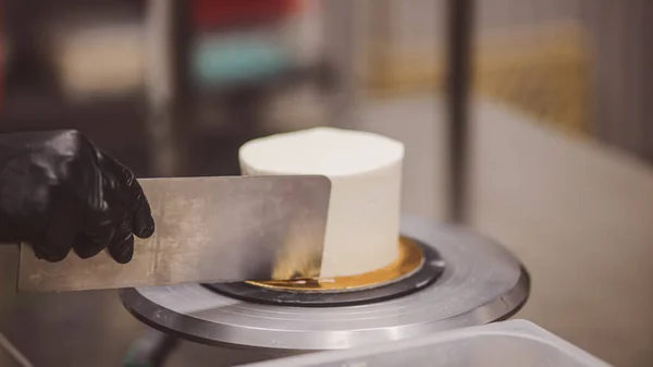 Decorator using spatula and scraper to smooth buttercream on a frosted cake