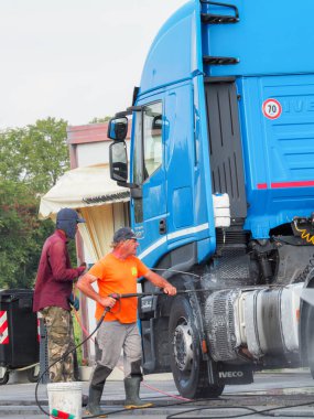 Adam, oto yıkamacıdaki self servis ekipmanlarını kullanarak mavi kamyonun dışını spreyliyor..